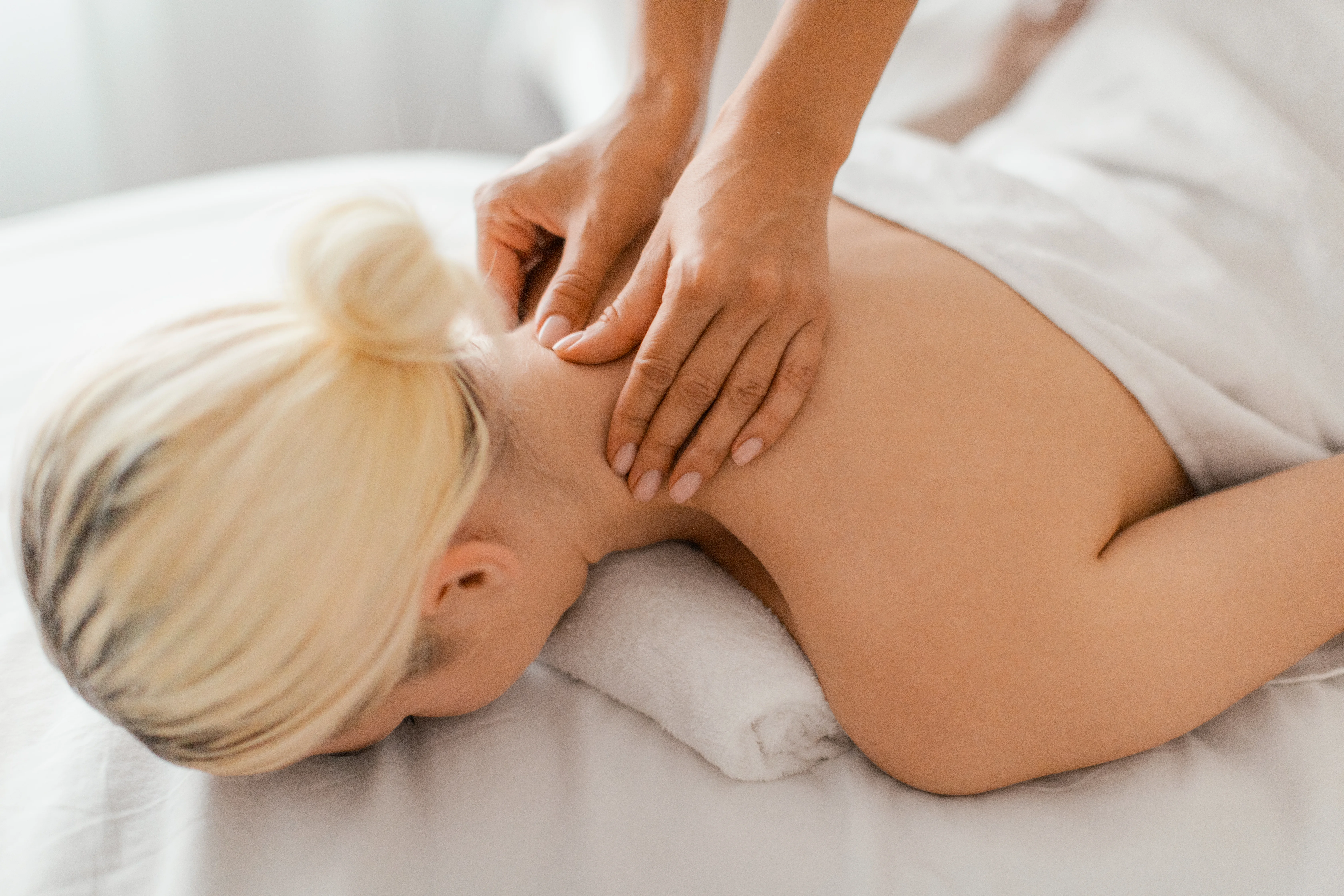 Close-up, landscape photo of a therapist giving a massage to the back of a woman's neck, illustrating relief from common neck pain and headaches.